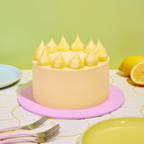 Classic Lemon Drizzle Cake by Crumbs & Doilies with smooth lemon buttercream and piped decoration on pastel cake board.